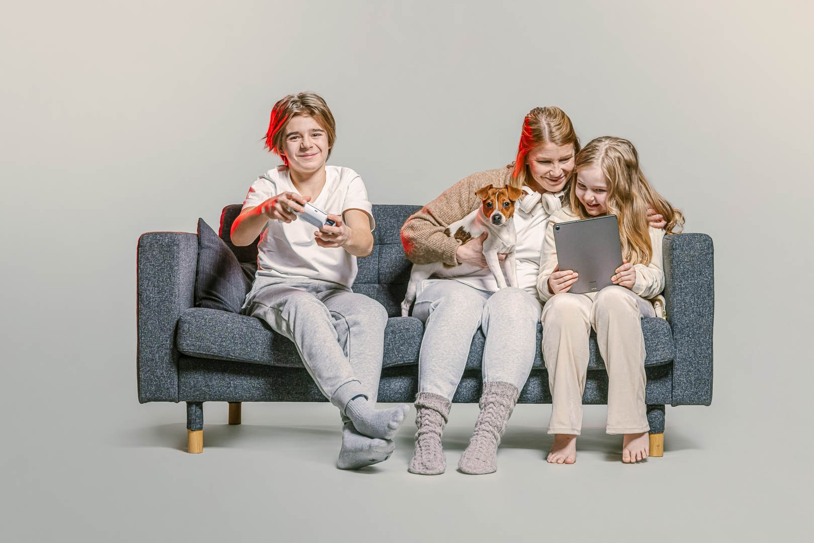 Äiti, lapsi ja koira istuvat sohvalla ja käyttävät älylaitteita.